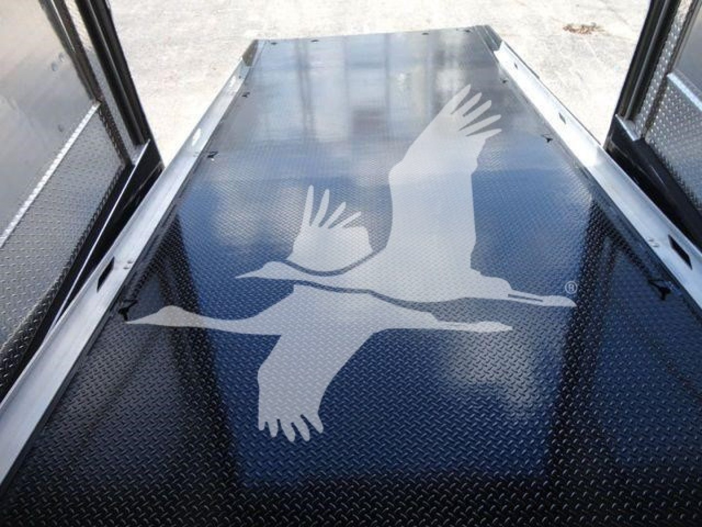 Truck trailer interior showing a diamond plate floor with a large white logo of a flying bird/leap in profile. The image also shows side rails and large back doors open.