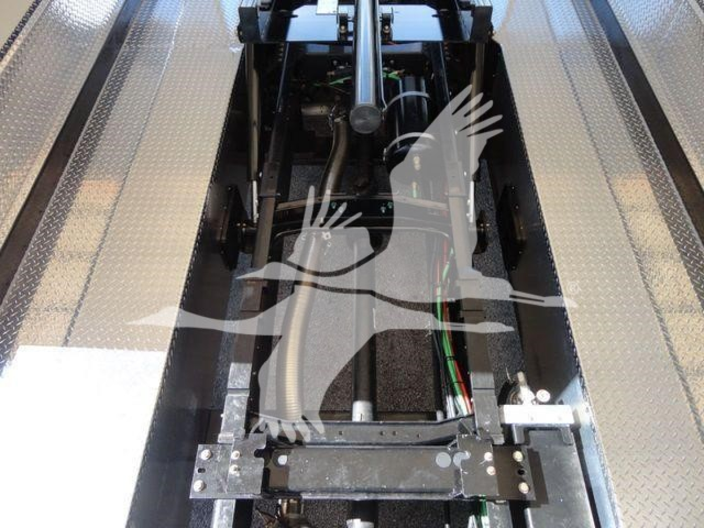 MD6 chassis area showing hydraulic lines and control linkage between platform rails; metallic diamond-plate side surfaces outline a central driveline section.
