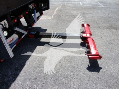 Mack MD6 rollback truck hitch attached to a trailer, red hydraulic arm at the end, with a steel hitch bar extending from a black trailer frame.