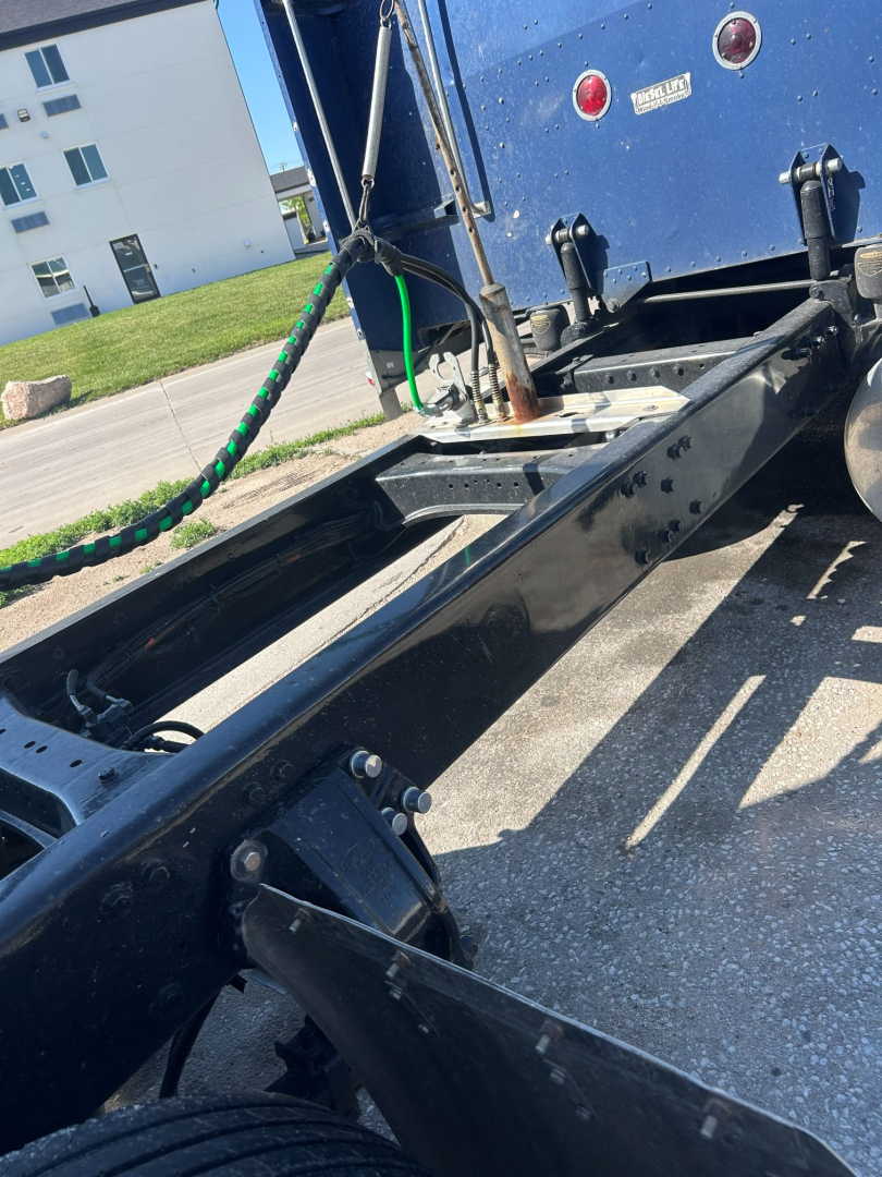 Truck chassis frame and fifth wheel area of a 2005 Peterbilt 379 EXT tractor showing frame rails, cab mounting, air lines, and rear area near the sleeper. Visible badges and blue paint.