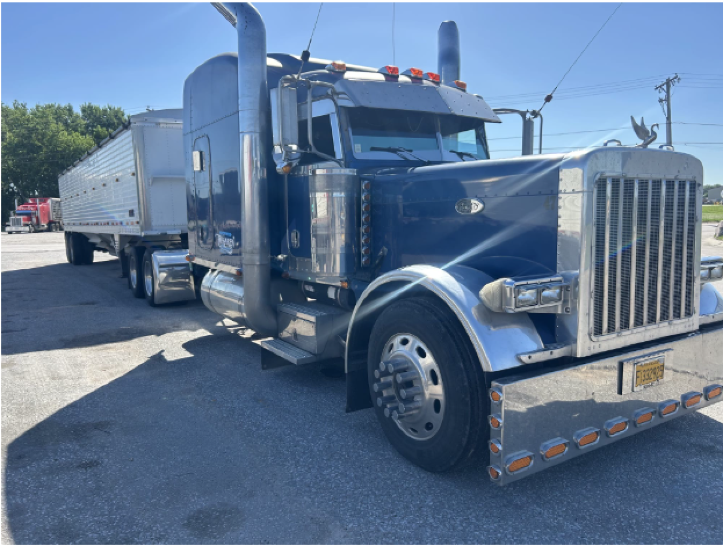 Peterbilt 379 EXT conventional sleeper truck with a blue exterior, long hood, dual exhaust stacks, chrome bumper guards, and a white trailer attached.