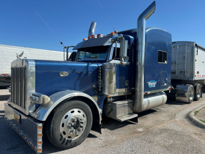 Peterbilt 379 EXT truck in blue with chrome exhaust stacks and sleeper cab. Visible text includes Peterbilt badge on grille and side of cab reading Peterbilt.