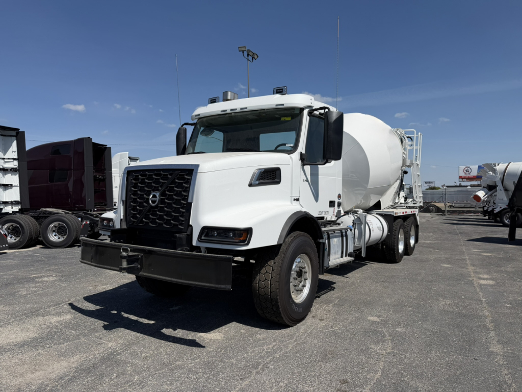 White Volvo VHD64B300 mixer truck with front bumper and cement mixer drum, side view, in a dealership lot.