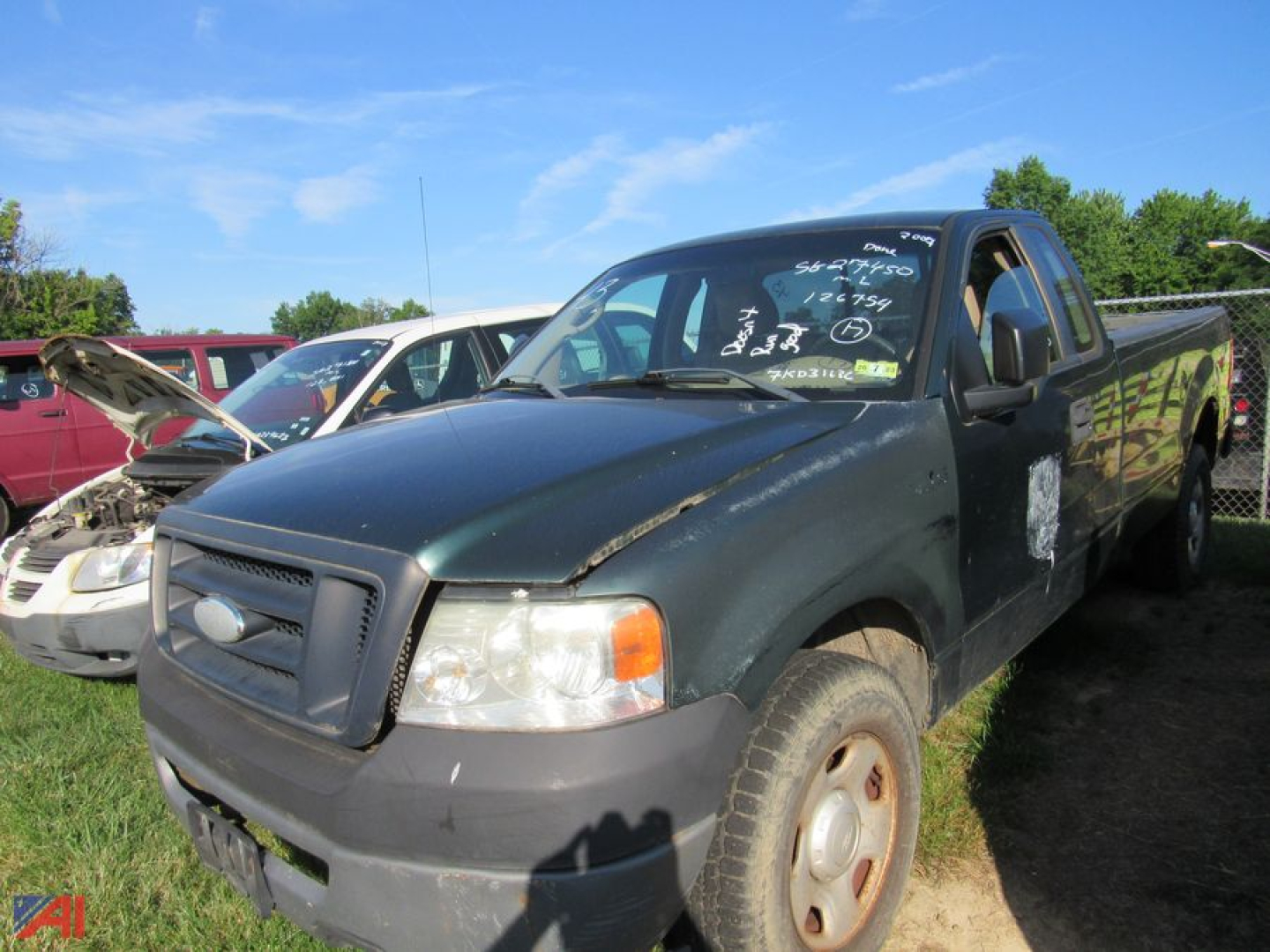 Ford F-150 pickup truck 2007 model in a used lot, dark green body, front-left view, writing on windshield, cargo bed, other vehicles in background.