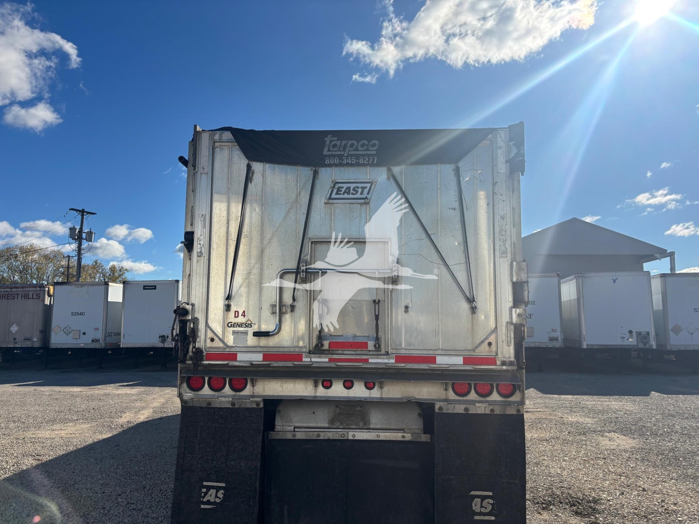 Rear view of a dump trailer with metal body and Taeco logo, Urn East branding, taeco, license plate missing, taillights, reflective tape, and bumper in a truck lot.