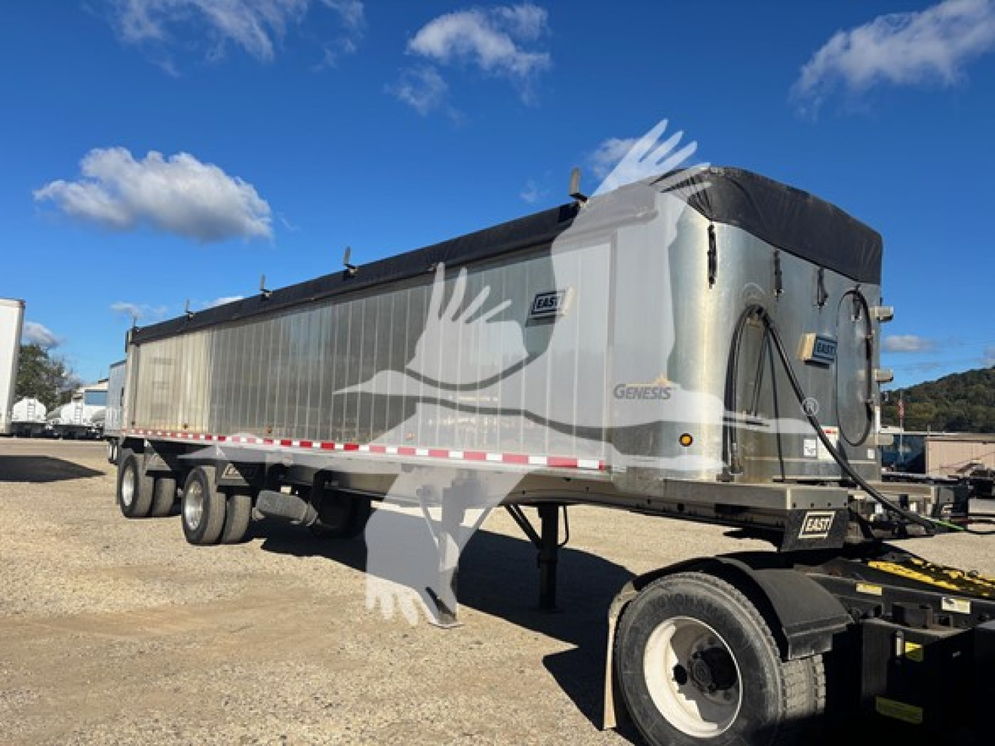 Trailer side view showing Genesis dump trailer with silver body and black tarp cover, tandem axles, and kingpin hitch.