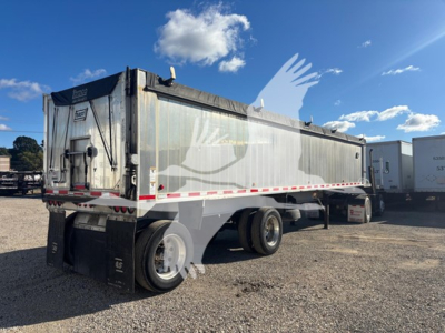 Trailer in a dump trailer yard showing side and rear with reflective tape, rear doors, dual rear wheels, and a black tonneau cover.