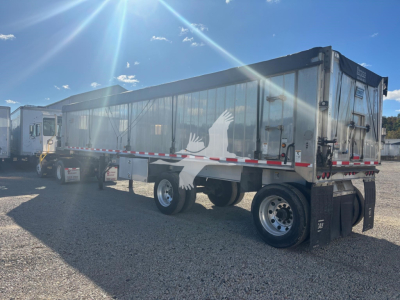 Trailer side view showing cargo trailer with painted eagle graphic and dual rear axles, East Hybrid dump trailer, VIN 1E1D2U288ER049667, stock 7487.
