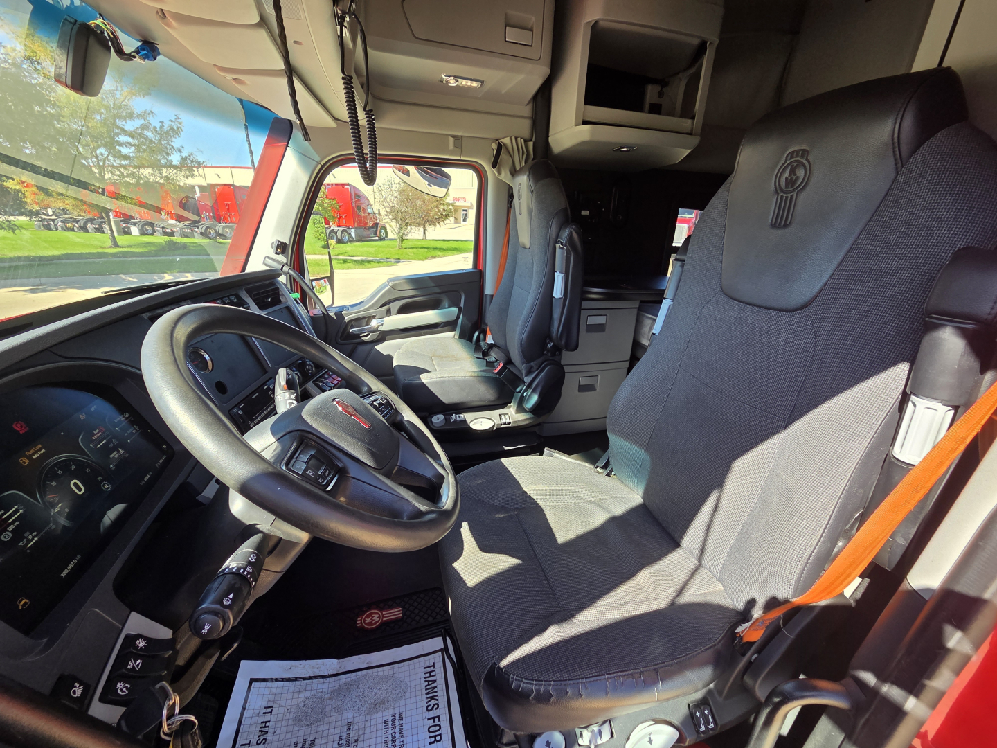 Kenworth T680 cab interior showing steering wheel and driver seat, dashboard, and passenger seat in view.