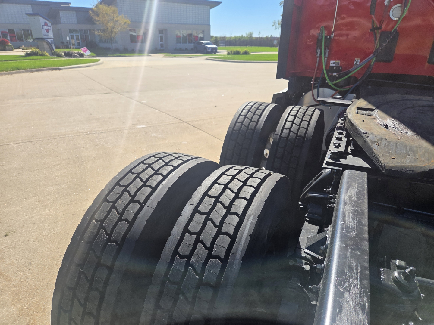 Kenworth T680 tractor rear dual tires and fifth wheel area showing tires and red cab; view focuses on rear axle and frame.