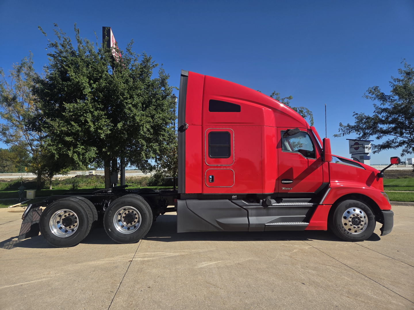 Kenworth T680 sleeper tractor side view showing red exterior and 3-axle rear with chrome wheels.