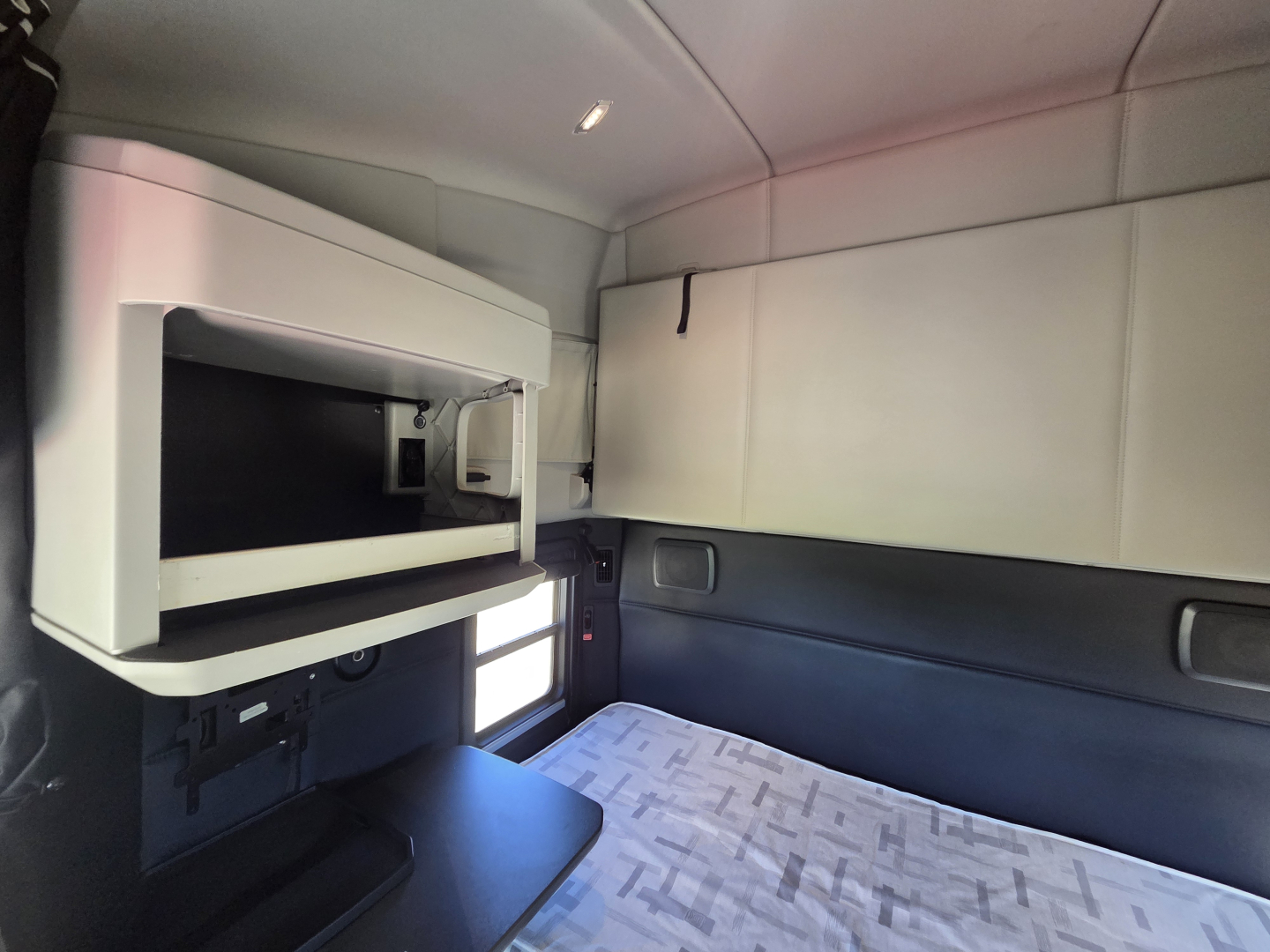 Kenworth T680 sleeper cab interior showing storage compartments and sleeping area with mattress and overhead cabinet.