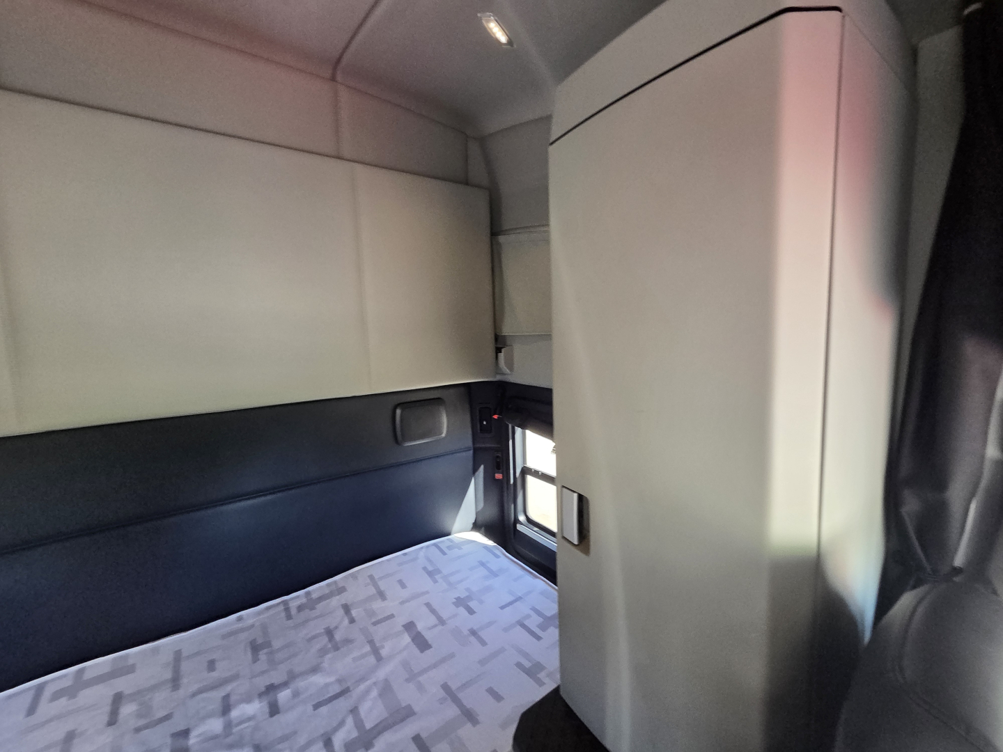 Kenworth T680 sleeper cab interior showing cabin partition and overhead storage with bed area.