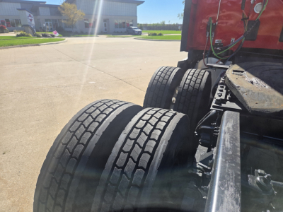 Kenworth T680 tractor rear dual tires and fifth wheel area showing tires and red cab; view focuses on rear axle and frame.
