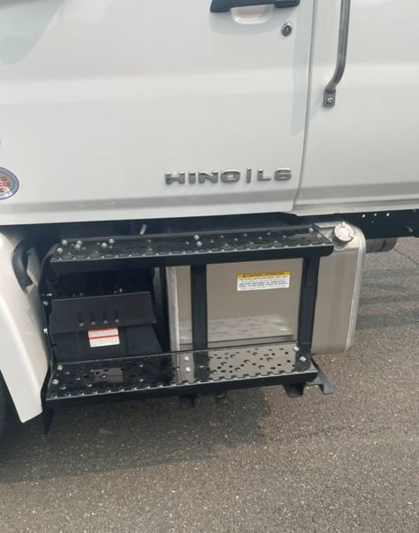 Truck side view showing Hino L6 badge, cab-chassis, side step/footboard and auxiliary battery compartment under door; visible step rails and black step with perforations.