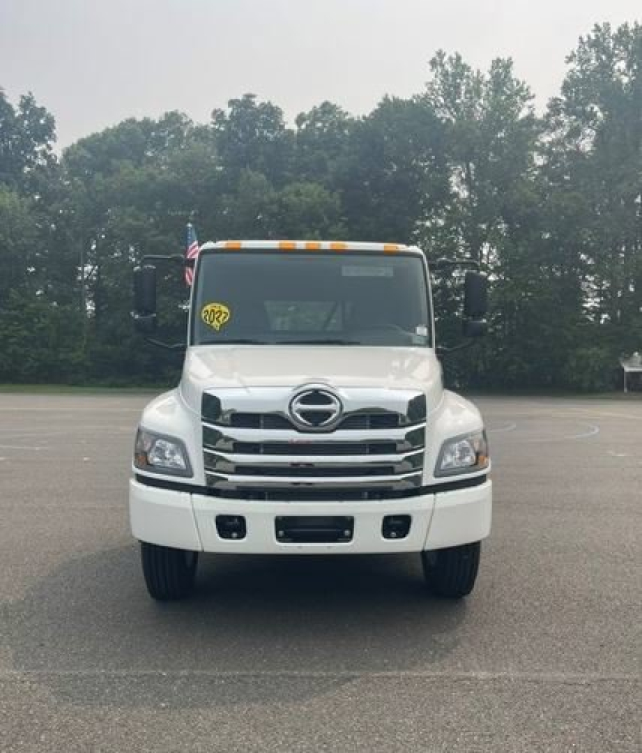 Front view of a white 2027 Hino L6 cab chassis truck with Hino emblem, chrome grille, and yellow inspection sticker on windshield.