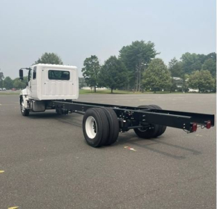 Truck cab chassis showing long wheelbase frame and dual rear axles with white cab and black frame.