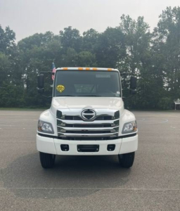 Front view of a white 2027 Hino L6 cab chassis truck with Hino emblem, chrome grille, and yellow inspection sticker on windshield.