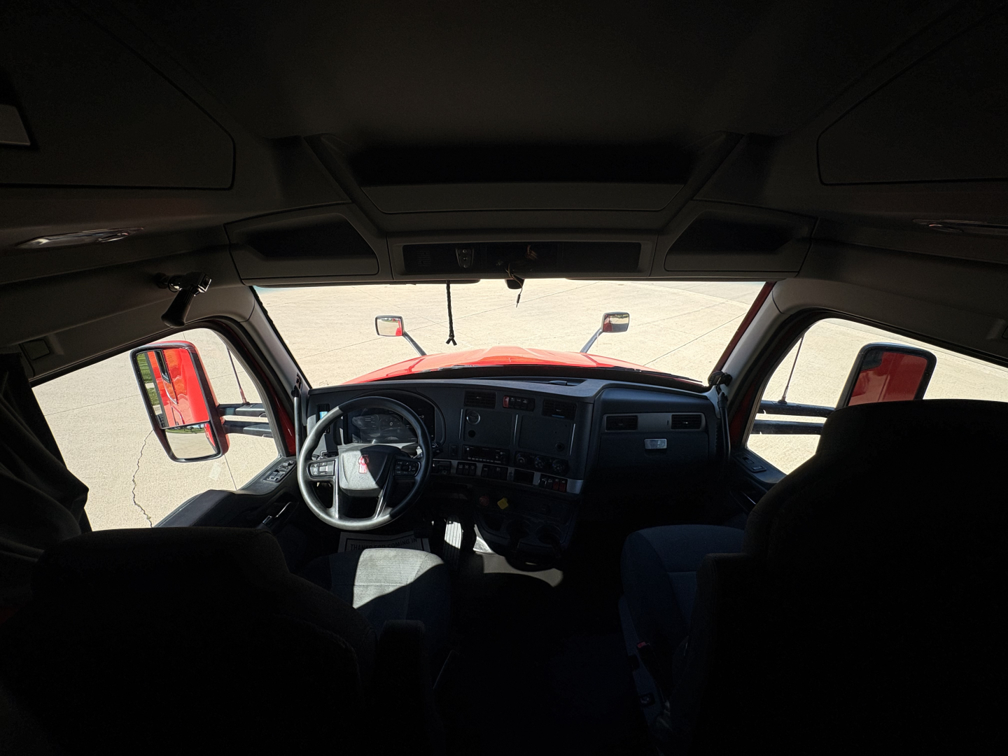 Kenworth T680 truck cabin interior view from driver seat showing steering wheel, dashboard, and windshield with side mirrors.