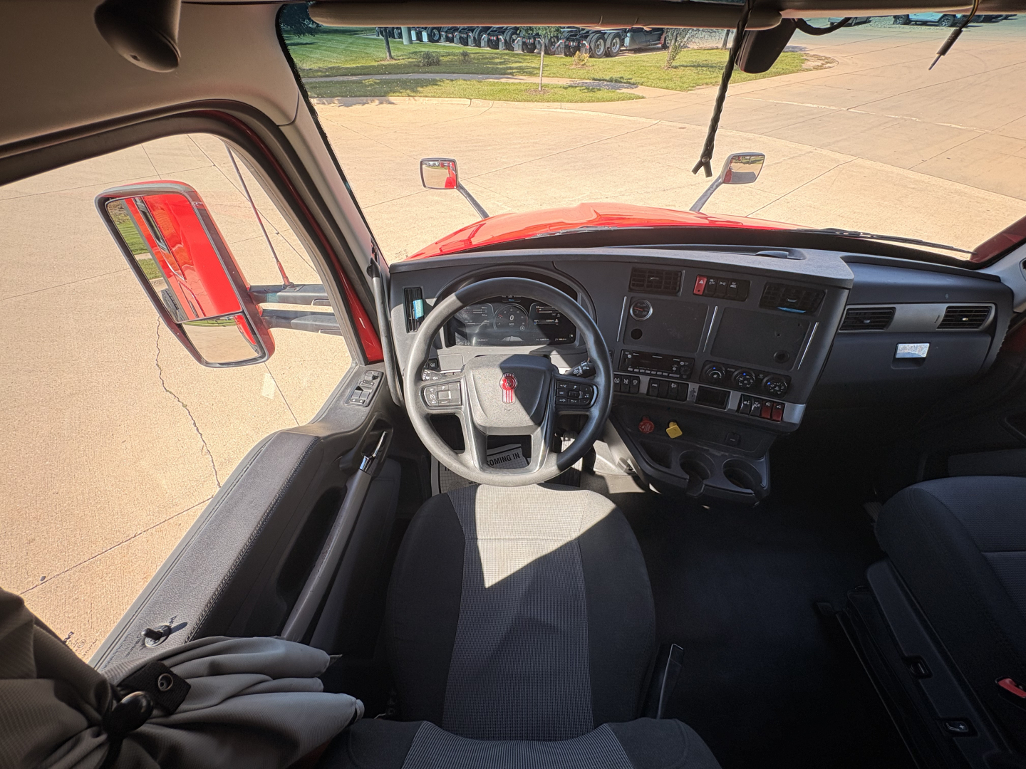 Kenworth T680 cab interior showing steering wheel and dashboard side view with red exterior door frame.