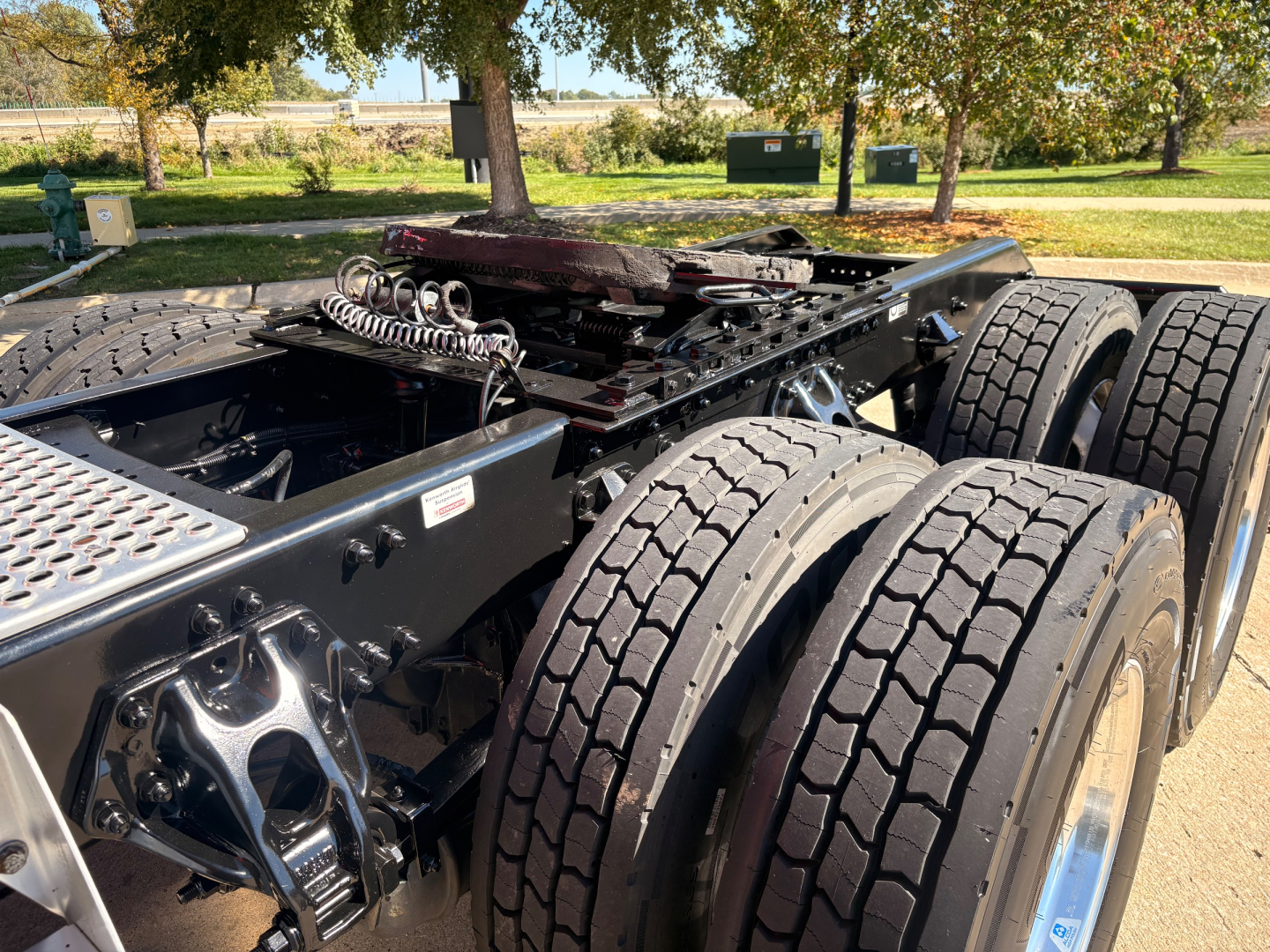 Kenworth T680 chassis with dual rear axles and exposed fifth wheel area showing suspension components and tires; no text legible other than vehicle frame details.