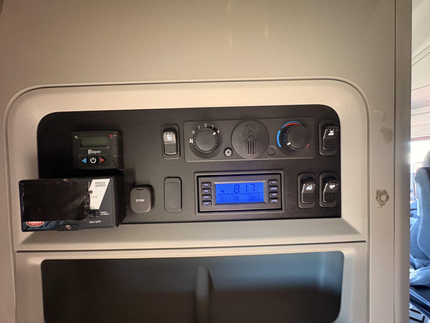 Kenworth T680 dash panel showing gauges, climate controls, blue-lit digital display, cigarette lighter style outlets, and a card reader slot.