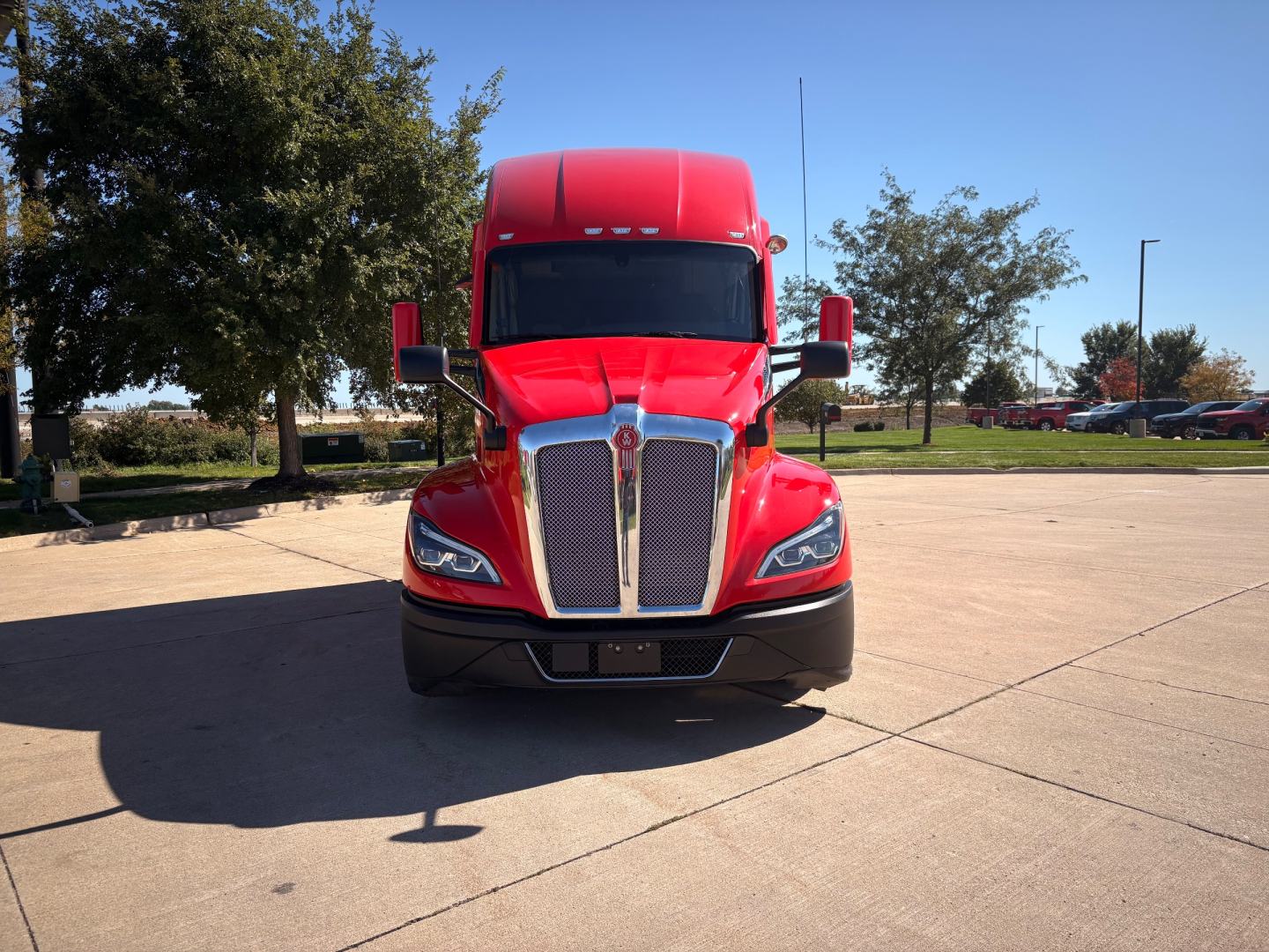 Kenworth T680 front view showing bold chrome grille, red paint, headlights, and side mirrors.