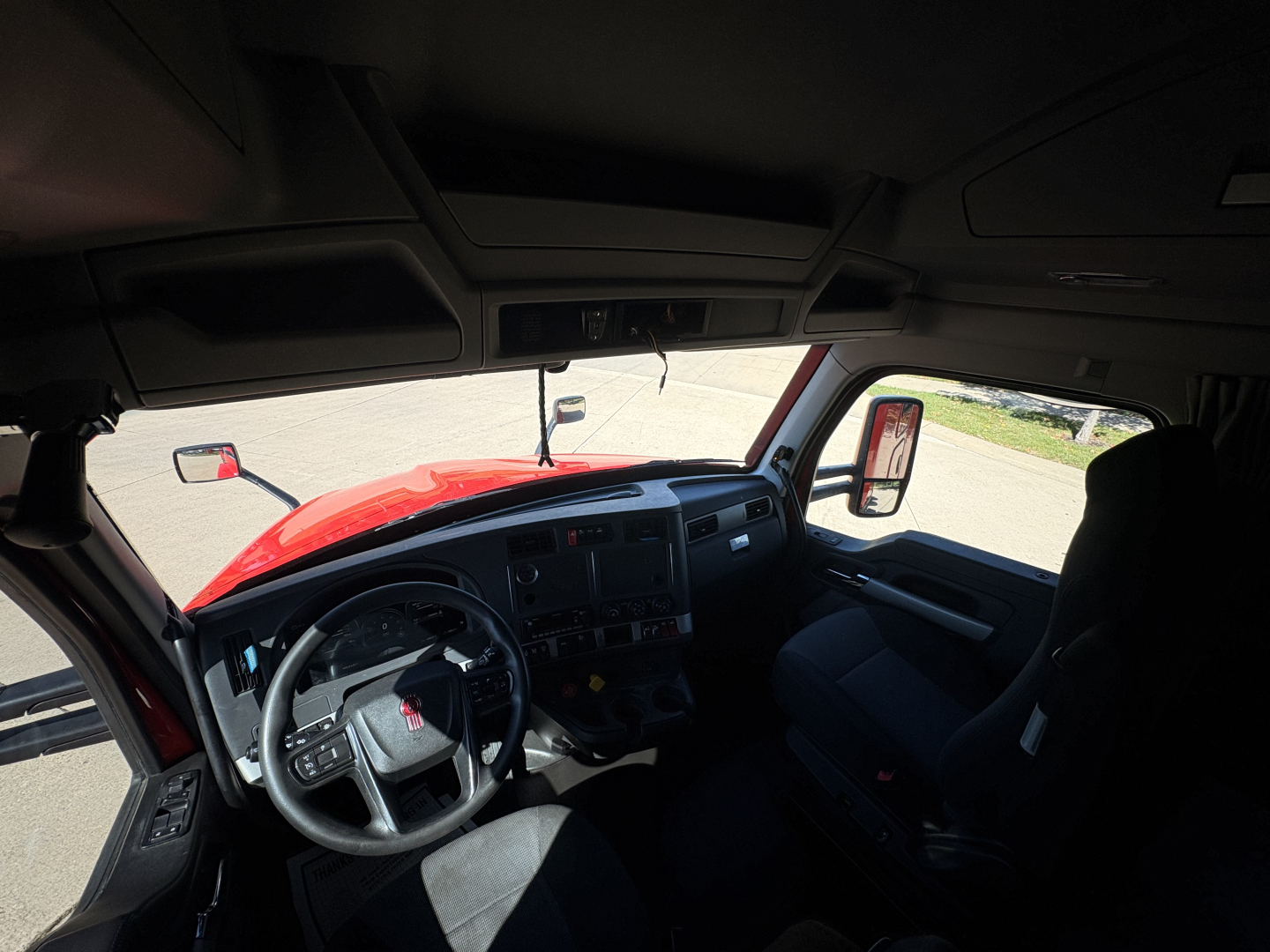 Kenworth T680 truck interior showing steering wheel, dashboard, and driver seat area from passenger side window view.
