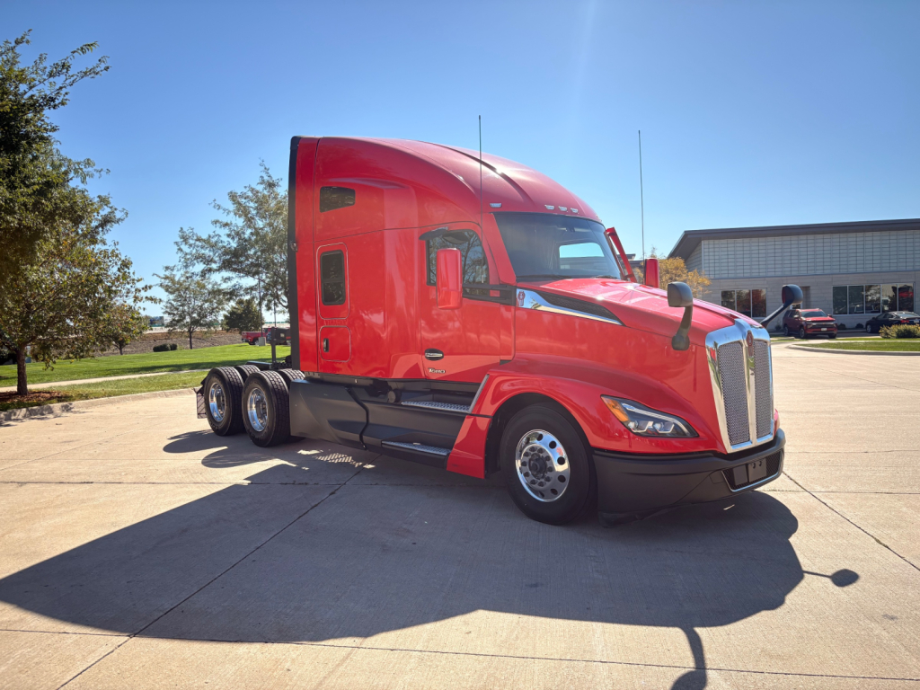 Kenworth T680 semi-truck in red with sleeper cab, three axles, daytime, dealership lot.