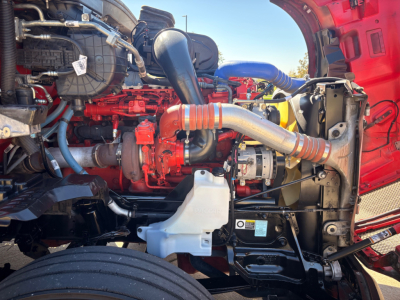 Kenworth T680 engine bay showing red engine, large intake hose, coolant reservoir, and surrounding components.