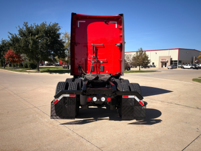 Kenworth T680 tractor rear view showing red cab interior and dual rear wheels with mudflaps and exhaust near trailer hitch.