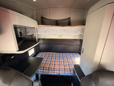 Kenworth T680 sleeper cab interior showing bunk beds and storage compartments, plaid bed setup, and cabinetry.