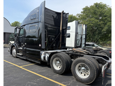 Volvo VNL 780 sleeper cab truck side view showing chassis and dual rear axles, black exterior, visible missing cab side panels, daytime outdoor dealer lot.
