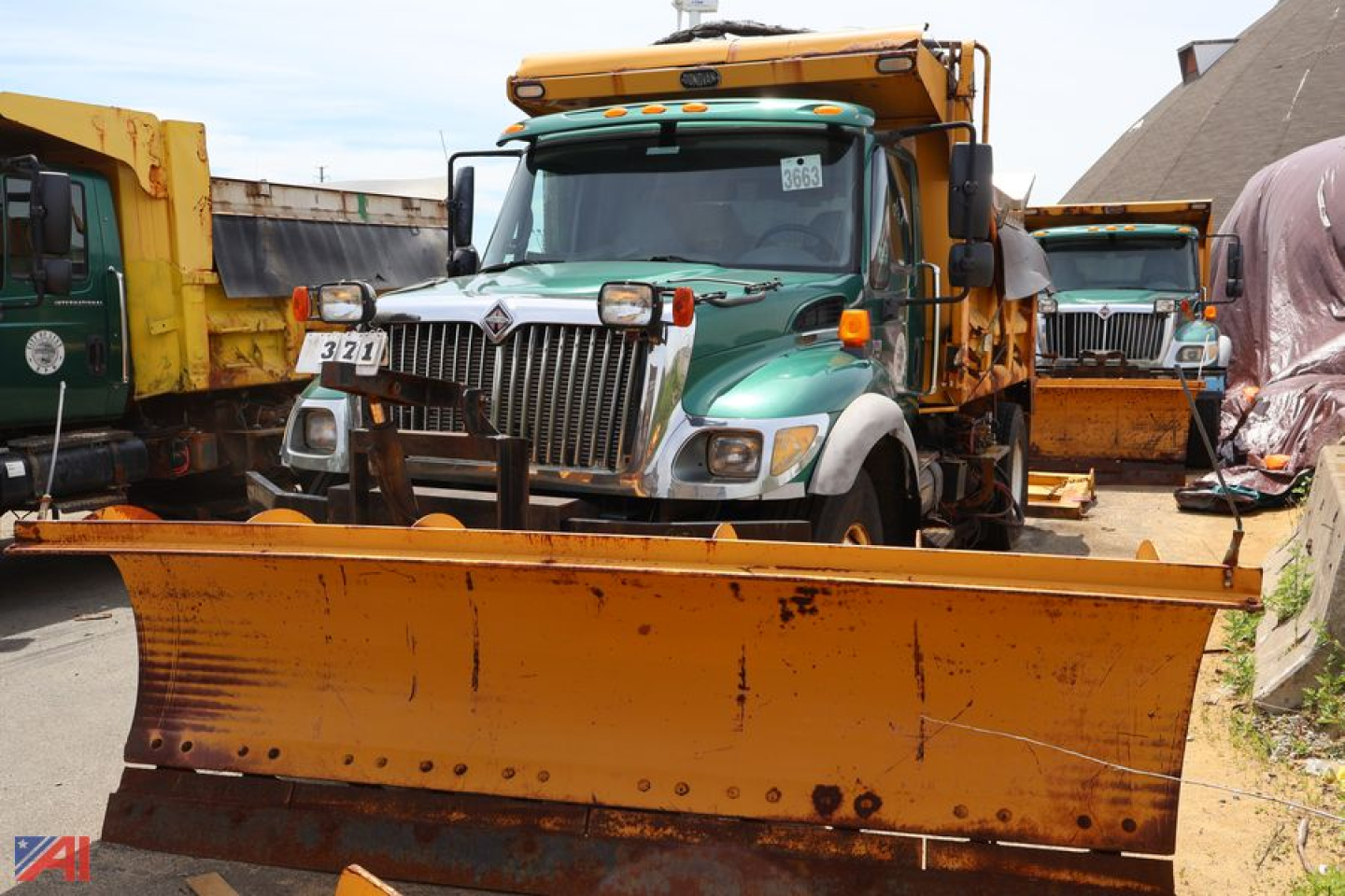 Front view of a green and white 2007 International WorkStar 7400 dump truck with a large orange snow/plow blade attached in front, other trucks in background.
