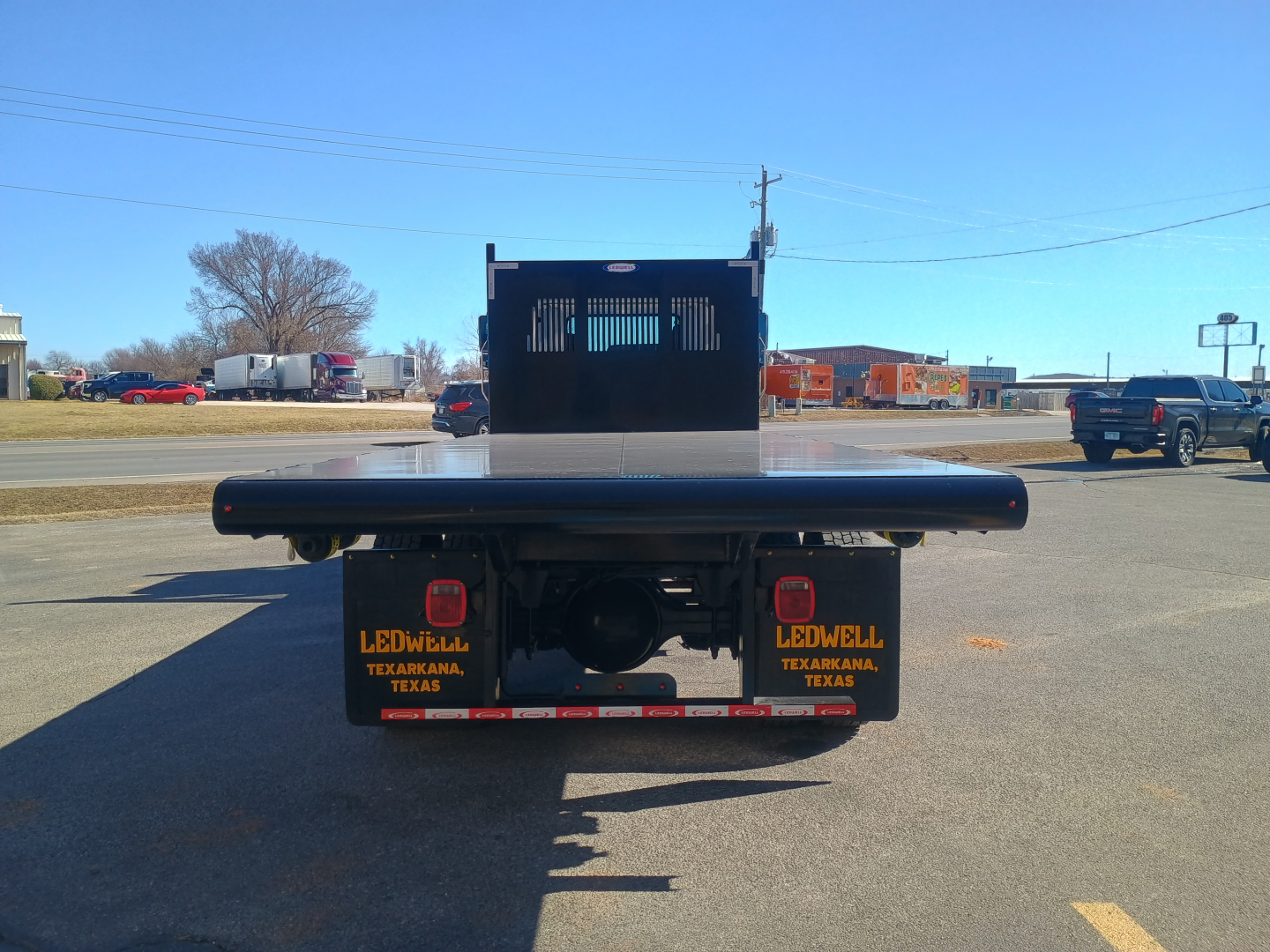 Truck flatbed rear view showing tail lights and license plate area with black mudflaps reading LEOWELL TEXARKANA TEXAS and a spare wheel housing.