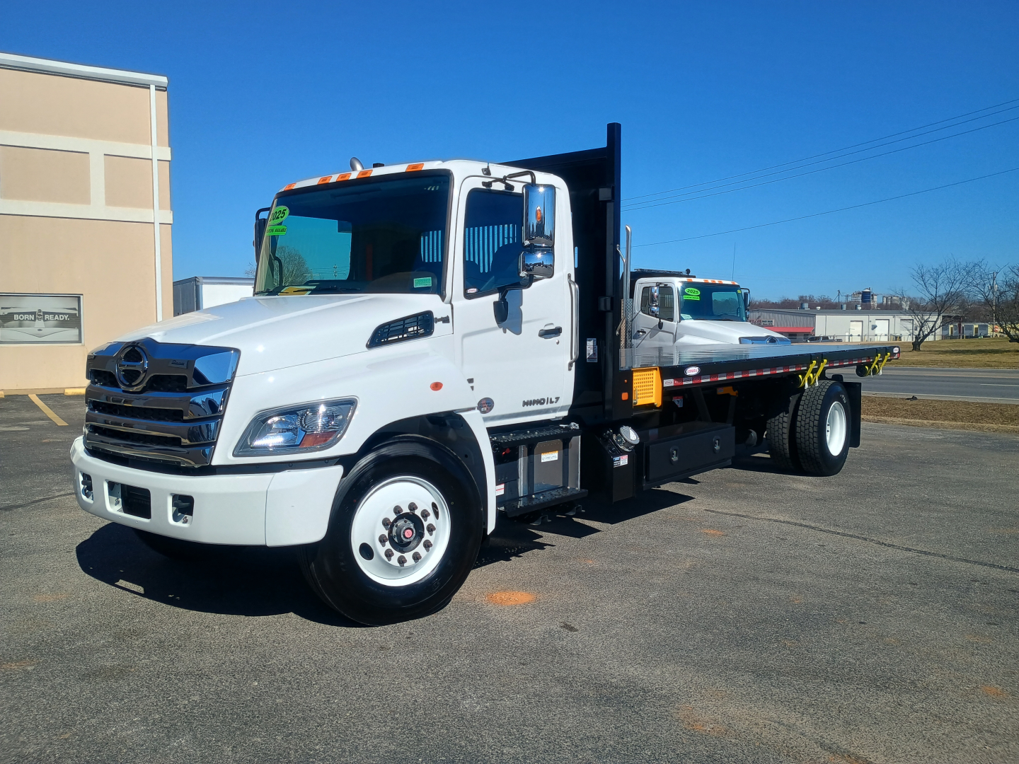 White 2025 Hino flatbed tow truck with a black flatbed and vertical crane, parked on lot.