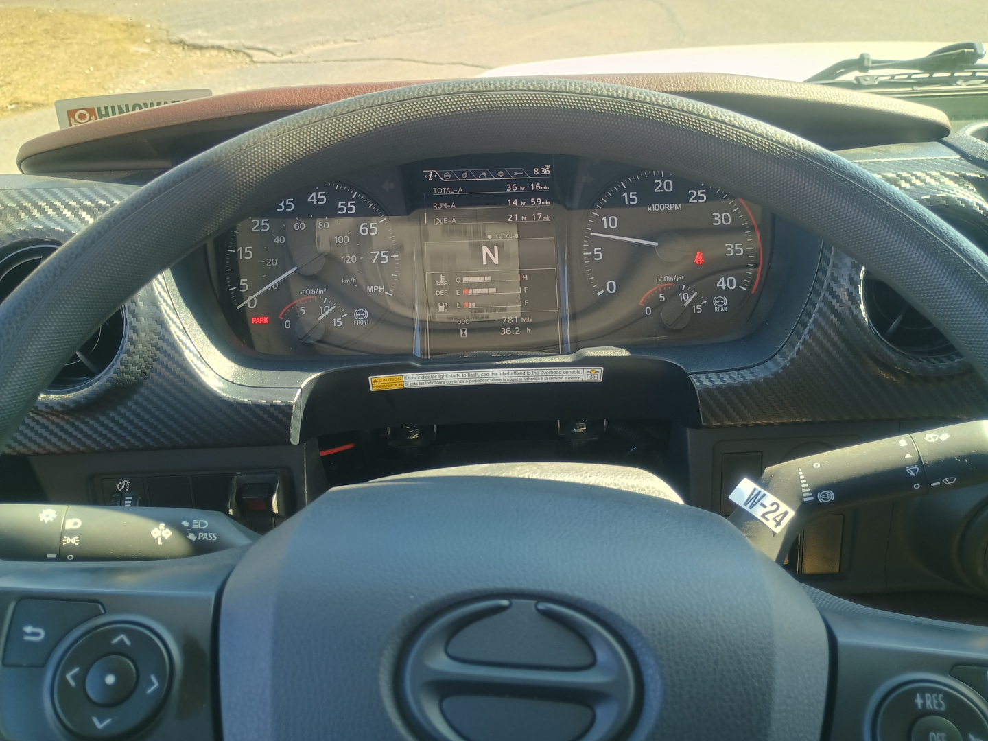 Dashboard view of a 2025 Hino L7 flatbed truck showing gauges and digital display with N gear indicator. Visible text includes numbers on the speedometer and tachometer, and a central display.