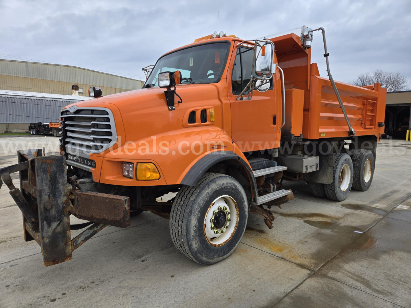 Orange Sterling LT9500 dump truck with front plow and dual rear wheels, side view showing dumping bed and cab.