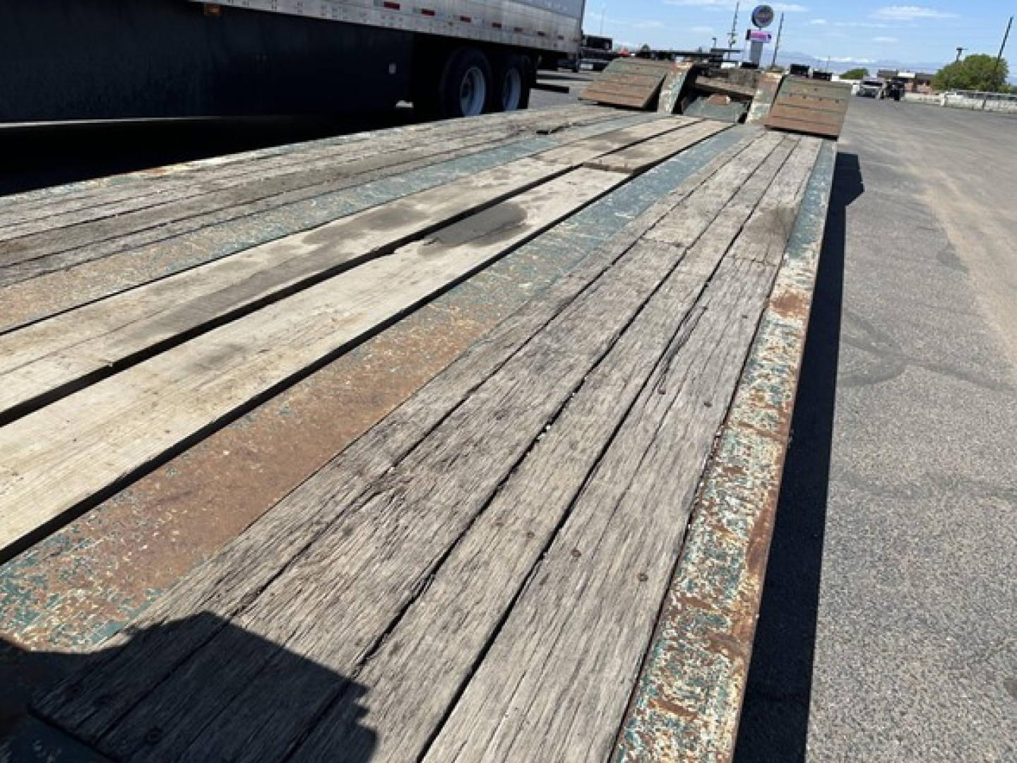 Trailer deck showing weathered wooden planks on a lowboy trailer with metal edge, long flatbed surface and ramp sections in background.