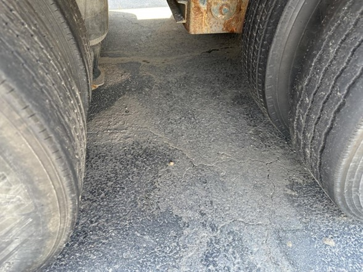 Lowboy trailer tandem axle view showing dual tires and dirt/grime on the ground between axles.