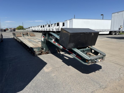 Lowboy trailer with flatbed sections and a black toolbox on the front, viewed from the side in a parking lot.
