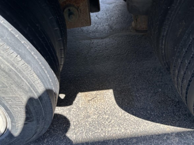Trailer wheel area showing dual rear tires on a Trail King lowboy trailer. Close-up view of tire treads and drum-like hubs with gravel surface underneath.