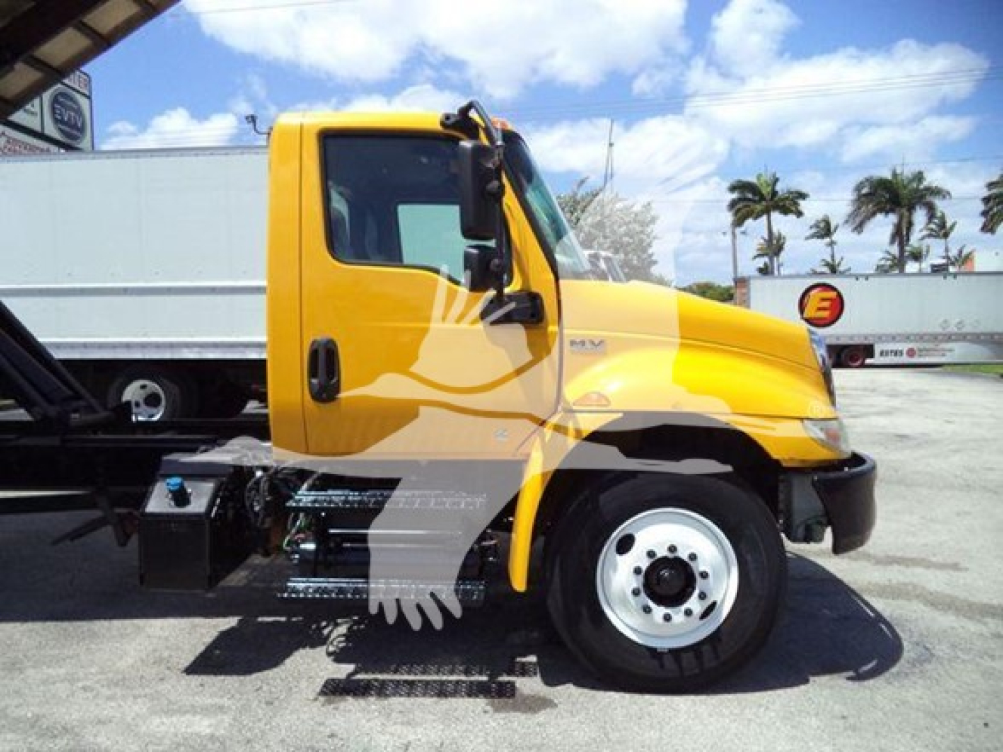 Truck cab side view of a yellow 2020 International MV with a chipper body, showing the driver door, wheel, and hydraulic components.