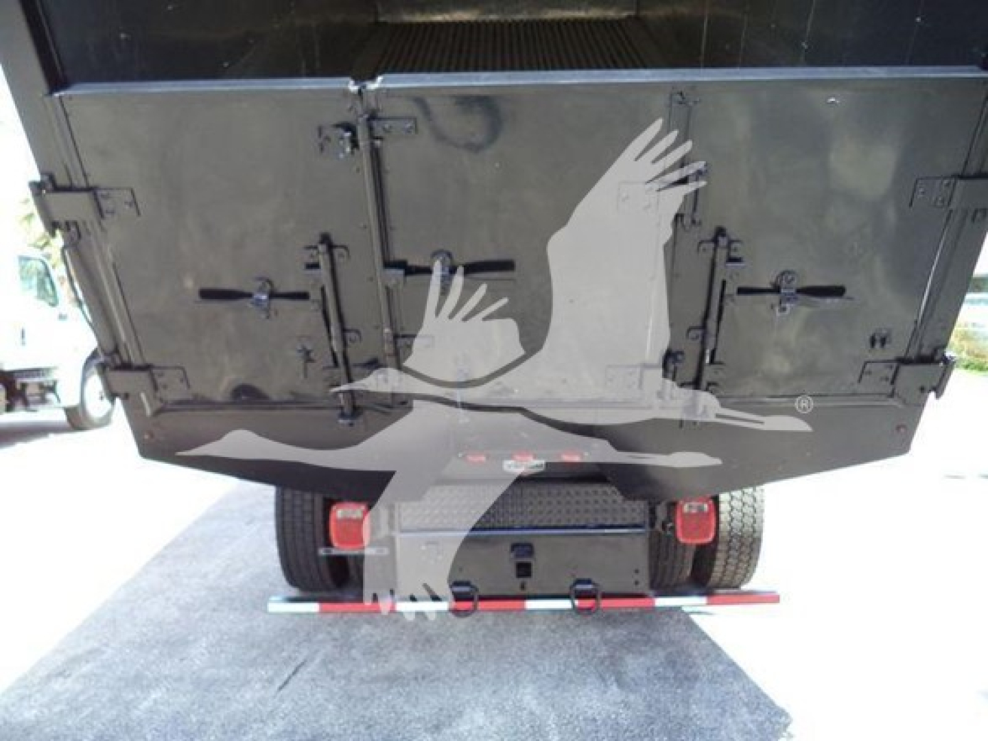 Chipper truck rear view showing heavy-duty tailgate with hinges and latches, bumper guide bar, and dual rear tires.