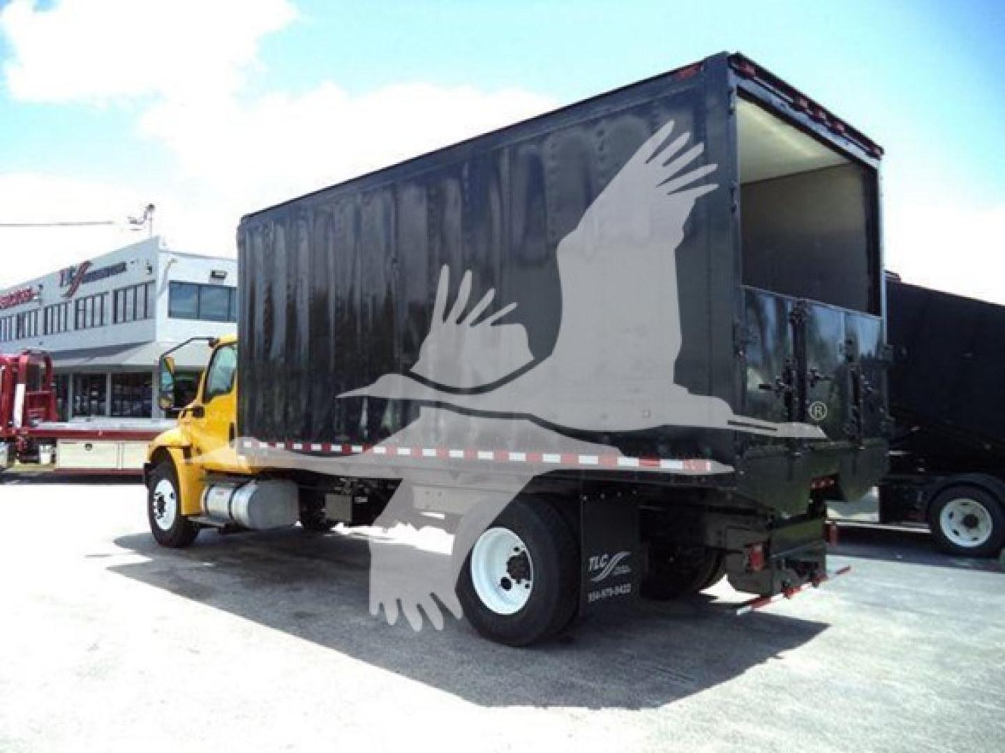 Box truck with a dark cargo box attached to a yellow cab; side shows a white flying bird logo. Open rear cargo door visible.