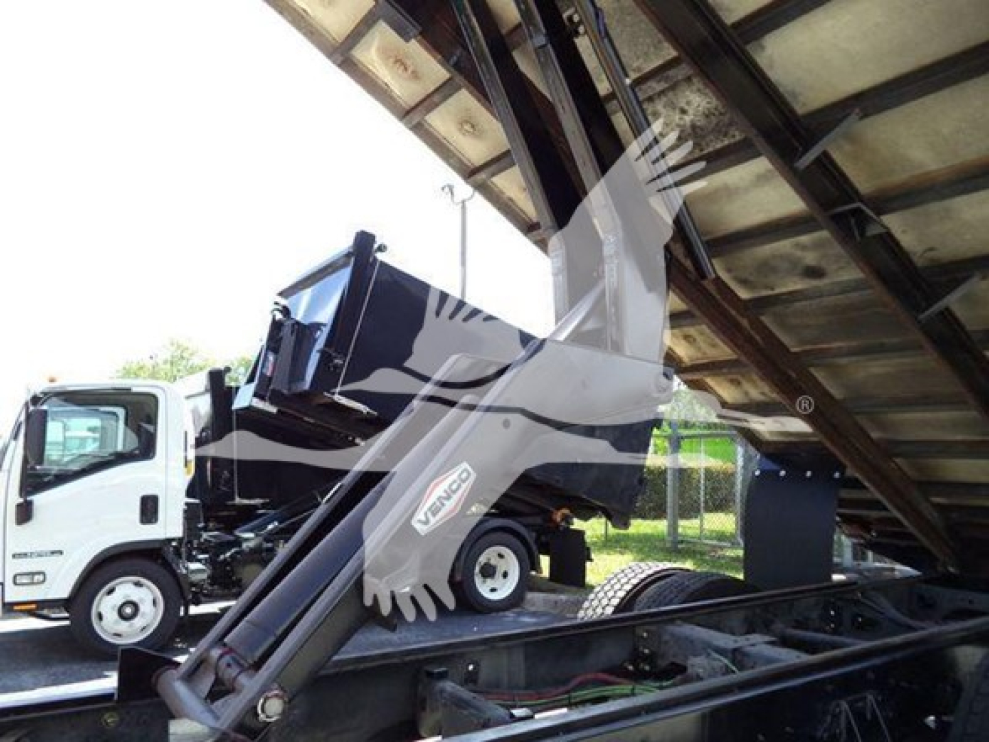 Truck with a hydraulic arm and dump bed inside a tilt trailer showing International MV branding