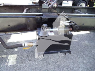 Chipper truck undercarriage showing hydraulic hose, control valve, and hydraulic reservoir fitted to frame rail.