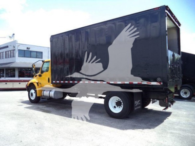 Side view of a yellow International truck with a large black box body, showing a white bird graphic on the cargo area.