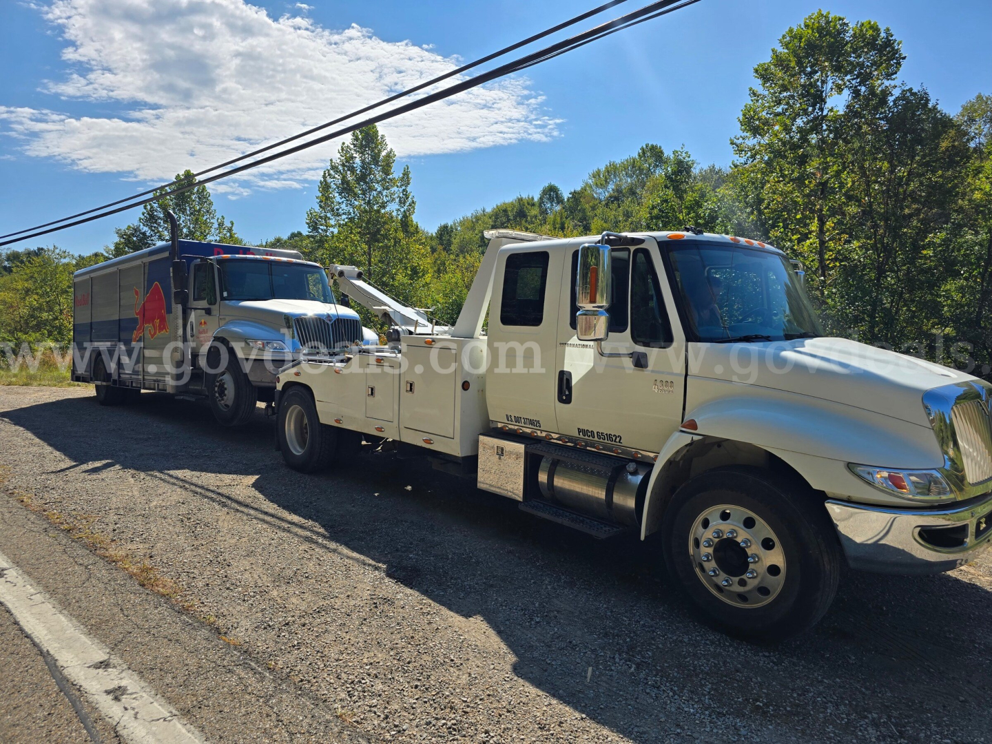 Tow truck setup showing a white International 4300 tow truck with a flatbed, connected to a larger blue tow vehicle in the background.