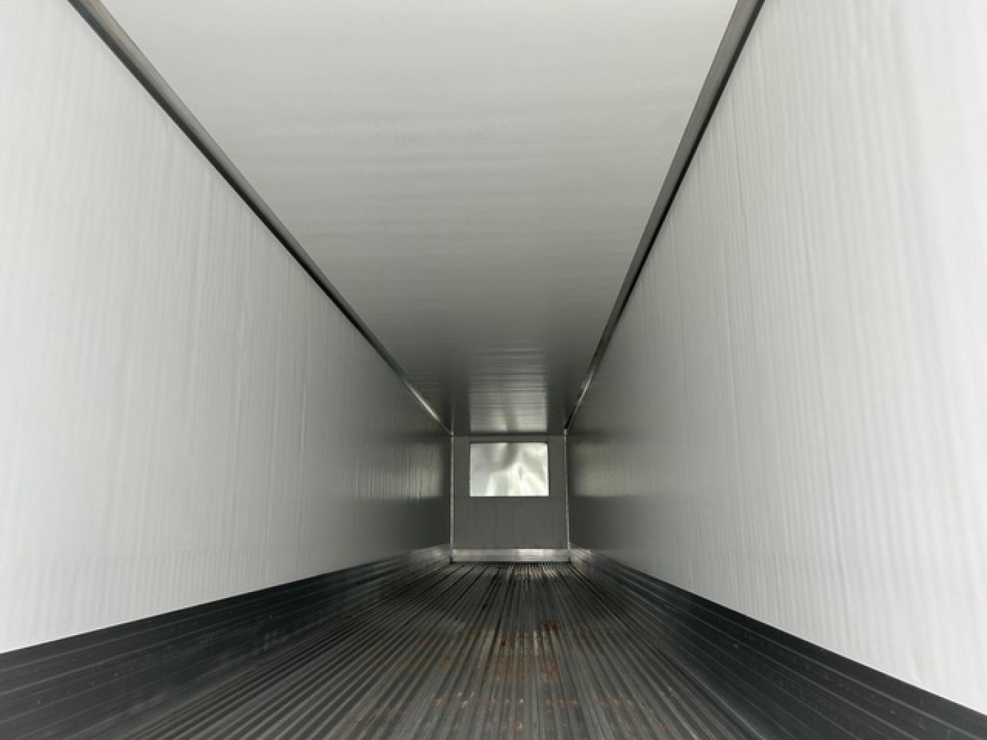 Interior of a refrigerated trailer showing clean metal walls and ribbed floor, with a small square window at the far end.